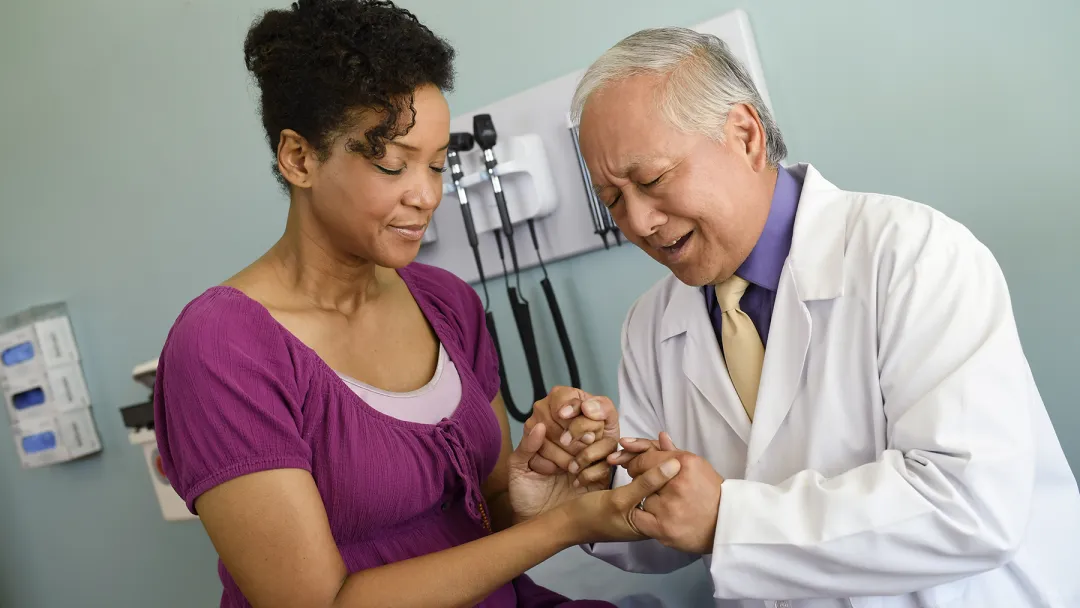 An Asian doctor prays with an African-American woman at the hospital.