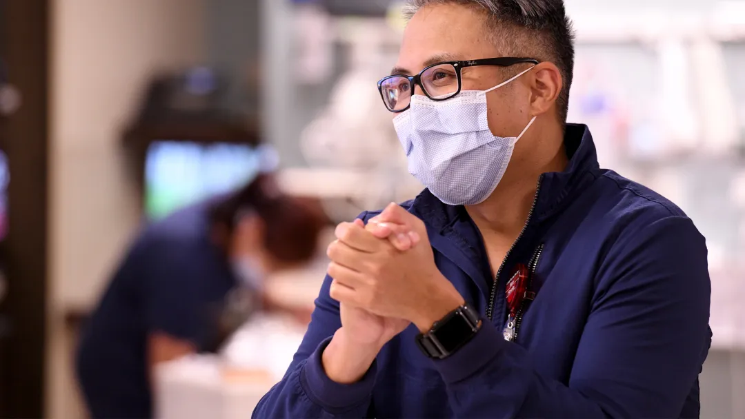 Man folding his hands together while wearing a mask.