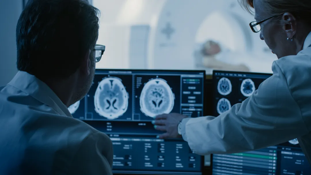 Radiologists looking at a brain scan while a patient is getting a CT scan.