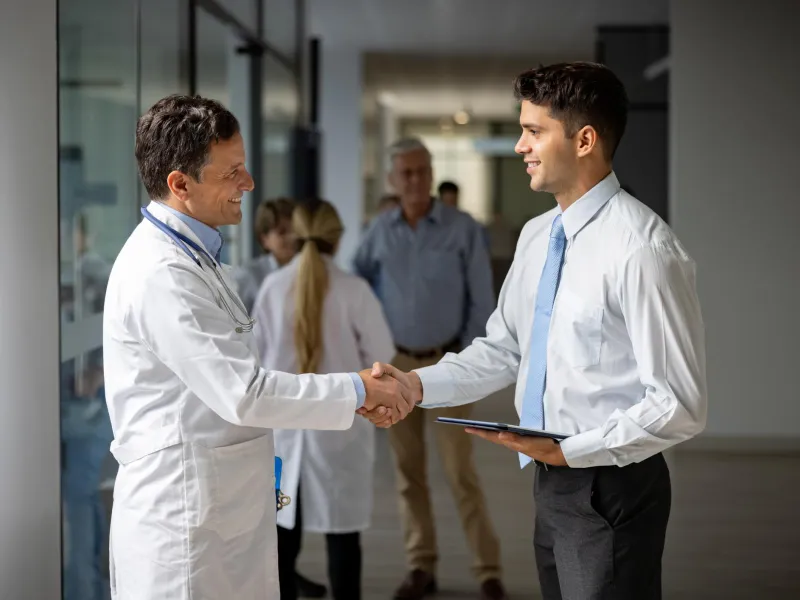 Young male intern shaking hands with a doctor in the hallway of a hospital.