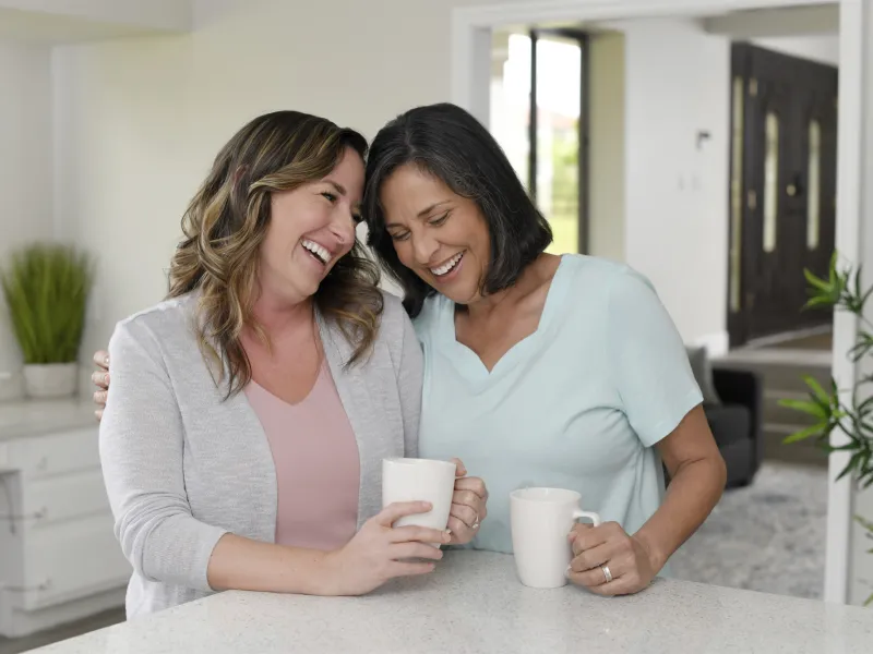 Two women laughing together in a kitchen.