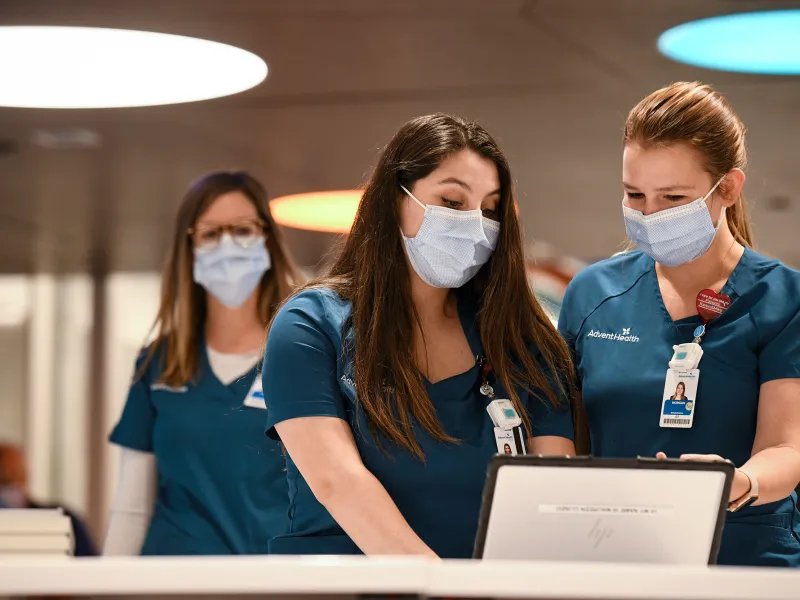 Two nurses looking at a laptop and talking while both wear masks.