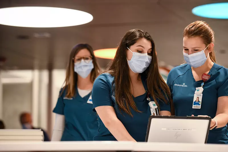 Two nurses looking at a laptop and talking while both wear masks.