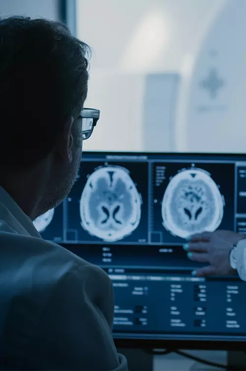 Radiologists looking at a brain scan while a patient is getting a CT scan.